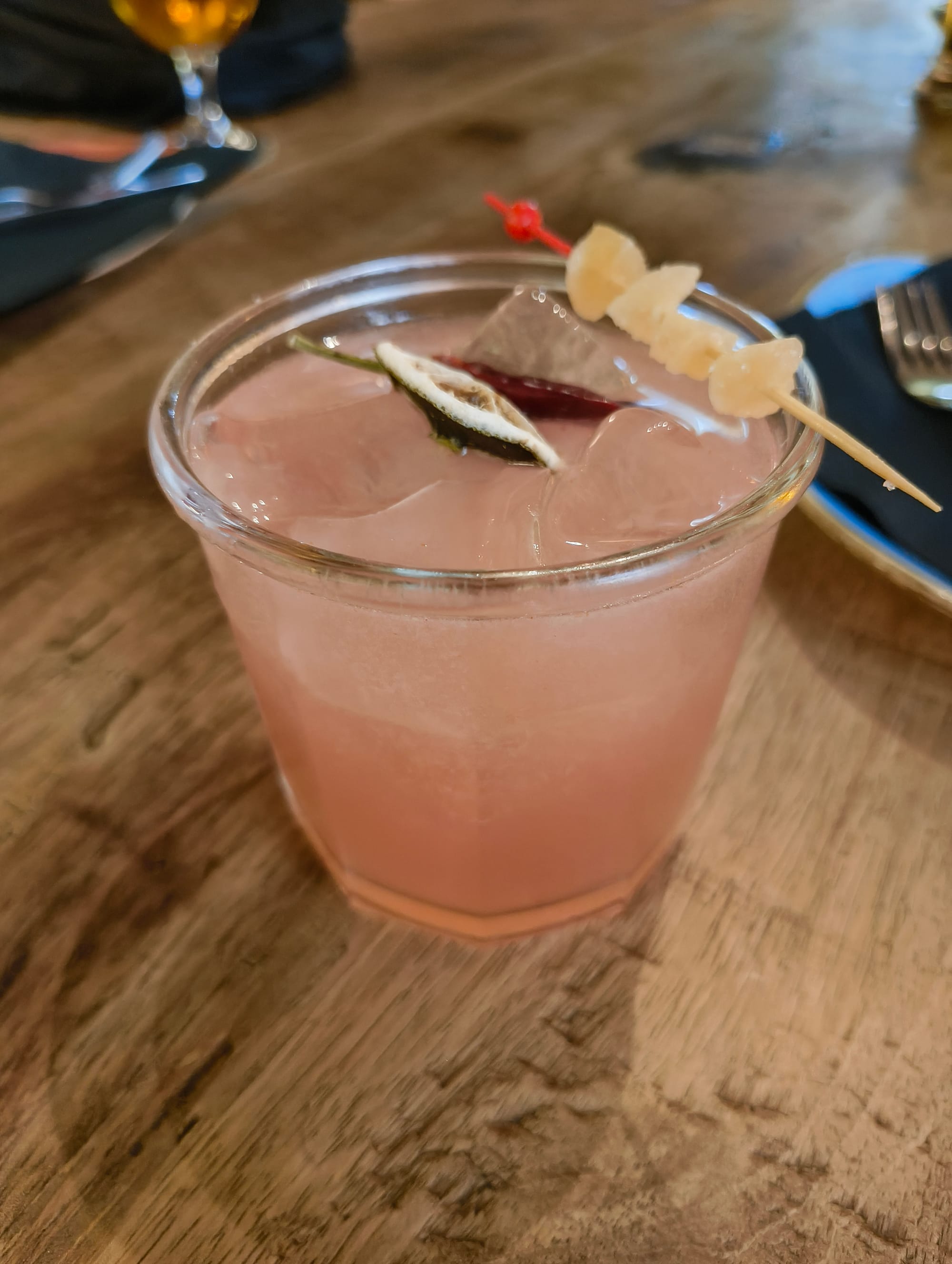 A pink liquid in a glass standing on the table. There are peppers and ginger placed on the glass.