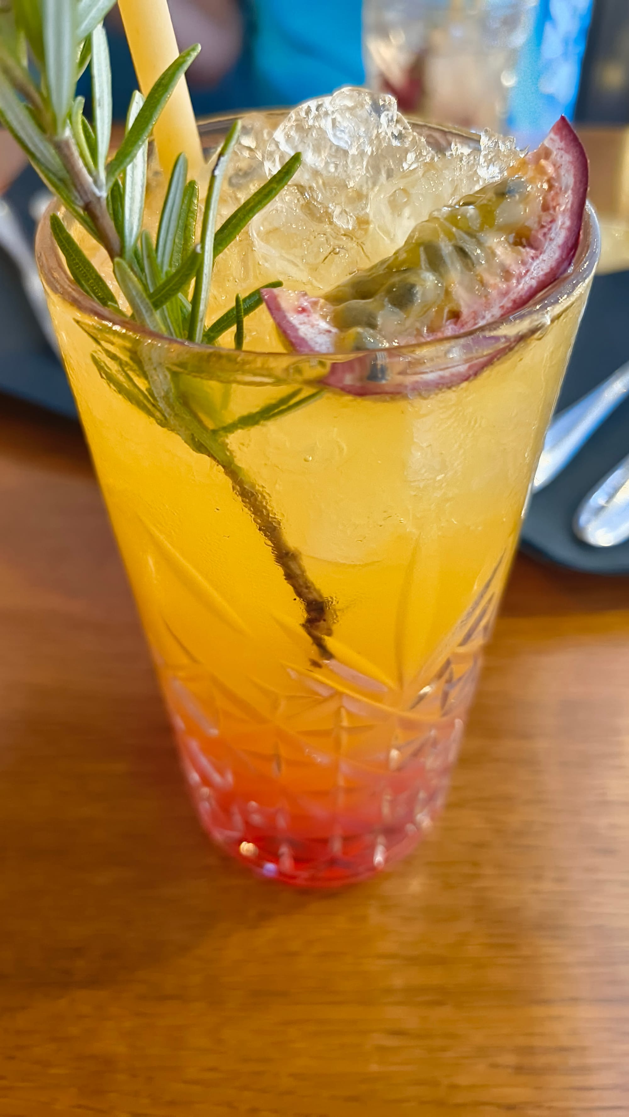 Orange and red liquid in a glass. Decorated with a passion fruit, ice and some green herb I forgot the name of.