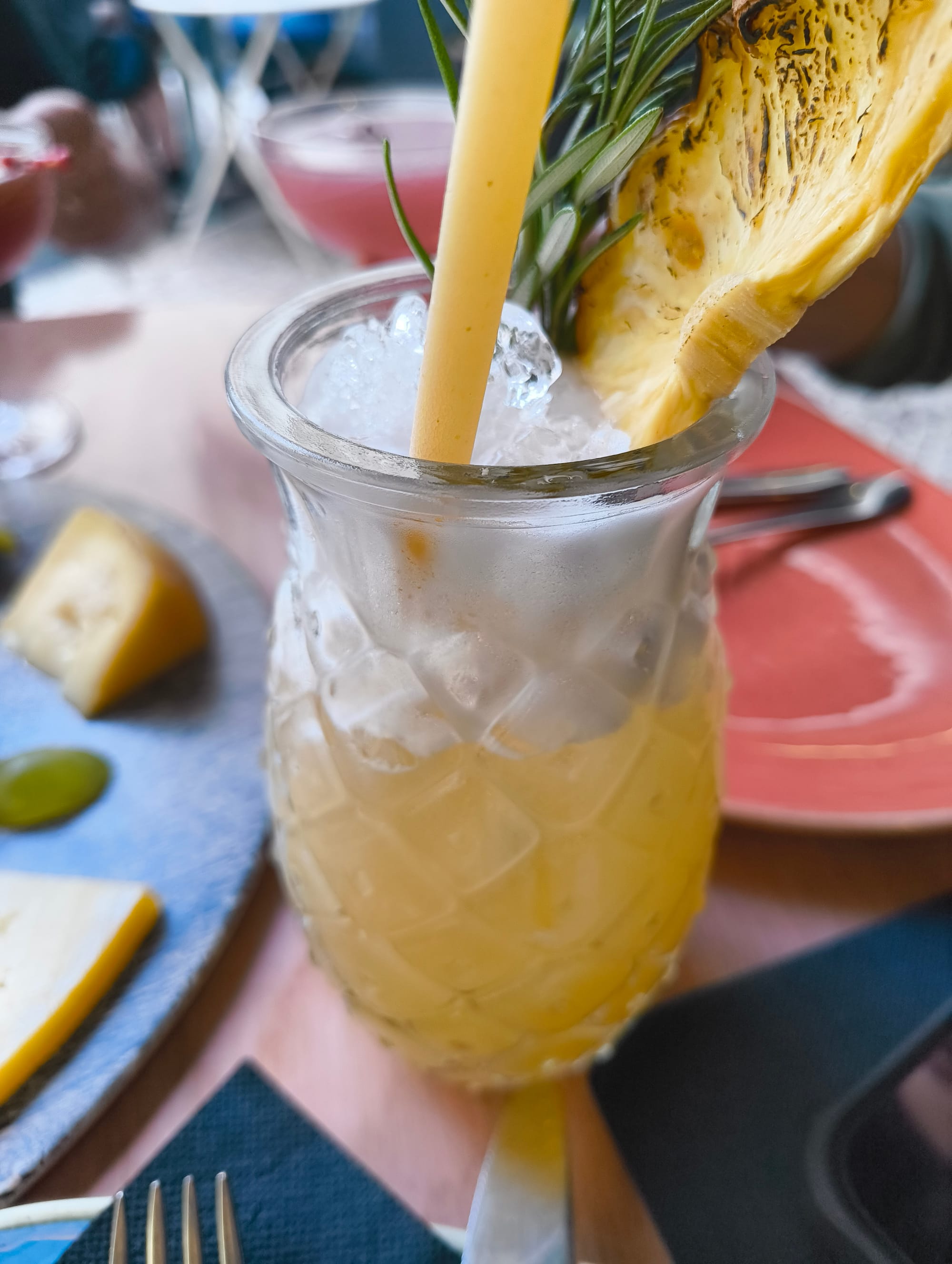 Orange liquid with white foam on top in a glass on a table. Decorated with a dried pineapple.