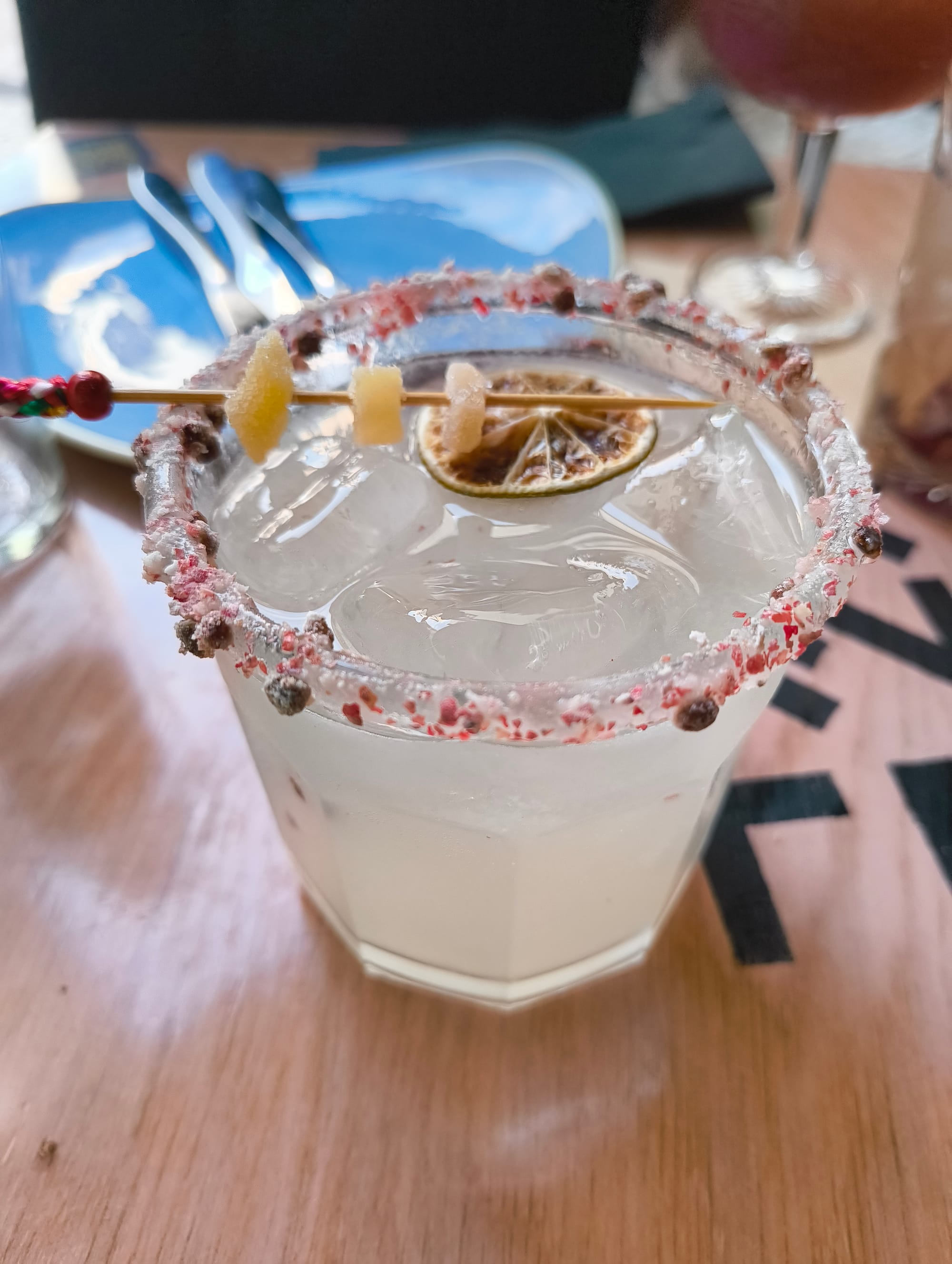 White liquid in a glass with a pink-pepper rim. Decorated with a dried lime and ginger.